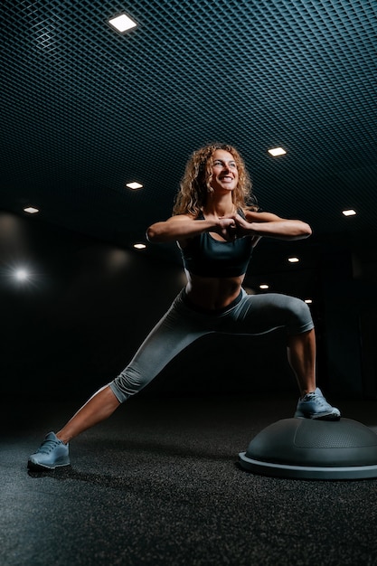 Sportowiec w siłowni w kolorze czarnym zajmuje się fitnessem, wykonując przysiady na platformie balansującej do głębokiej mus...