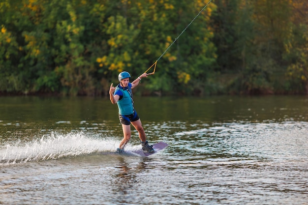 Sportowiec wykonuje trik w parku wodnym o zachodzie słońca. Jeździec na wakeboardzie