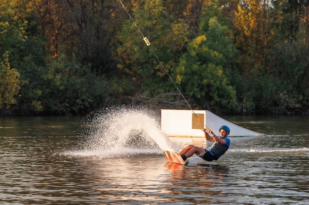 Sportowiec wykonuje trik w parku wodnym o zachodzie słońca. Jeździec na wakeboardzie