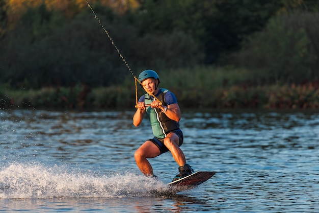 Sportowiec wykonuje trik w parku wodnym o zachodzie słońca. Jeździec na wakeboardzie