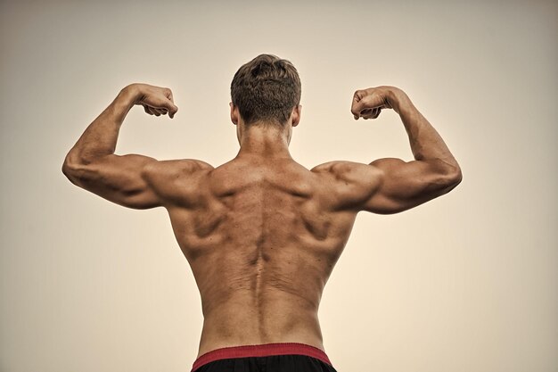 Zdjęcie sportowiec z gołym tułowiem na szarym niebie kulturysta pokazujący mięśnie biceps i triceps człowiek lub sportowiec zgięty rękami pięściami z tyłu widok fitness i sport zdrowy styl życia koncepcja