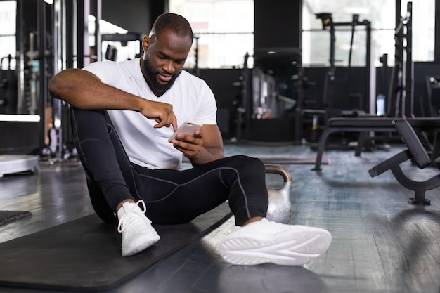 Sportowy afrykański mężczyzna odpoczywający patrząc na telefon po przerwie po ćwiczeniach