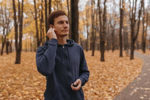 Sportowy biegacz słuchający muzyki w słuchawkach bezprzewodowych podczas treningu w jesiennym parku