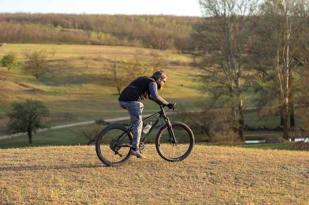 Sportowy brutalny brodaty facet na nowoczesnym rowerze górskim Rowerzysta na zielonych wzgórzach na wiosnę