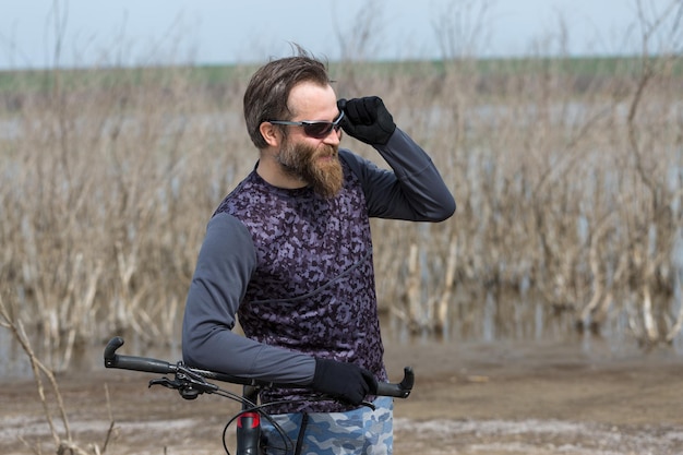 Sportowy brutalny brodaty facet na nowoczesnym rowerze górskim Rowerzysta w opuszczonym przez sól miejscu nad jeziorem