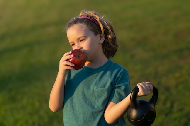 Sportowy dzieciak z jabłkiem i kettlebell na świeżym powietrzu w letnim parku Ćwiczenia sportowe dla dzieci Koncepcja zdrowego życia i sportu dla dzieci Motywacja i koncepcja sportu dla dzieci