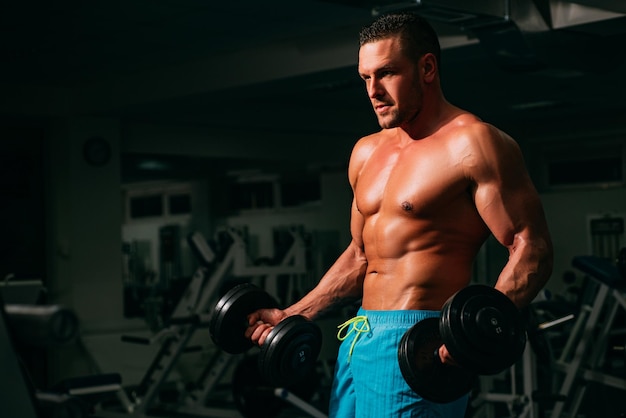 Sportowy mężczyzna robi biceps podnoszenia na siłowni Młody muskularny mężczyzna z nagim torsem ćwiczy w siłowni Atletyczny mężczyzna sportu