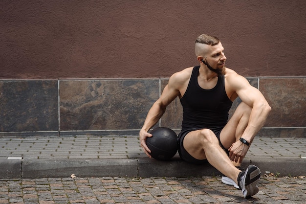 Sportowy mężczyzna siedzi z piłką do ćwiczeń na zewnątrz