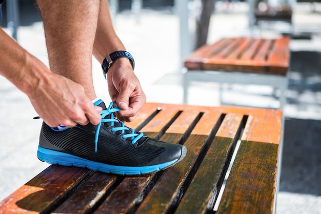 Zdjęcie sportowy mężczyzna wiąże jego shoelaces na ławce