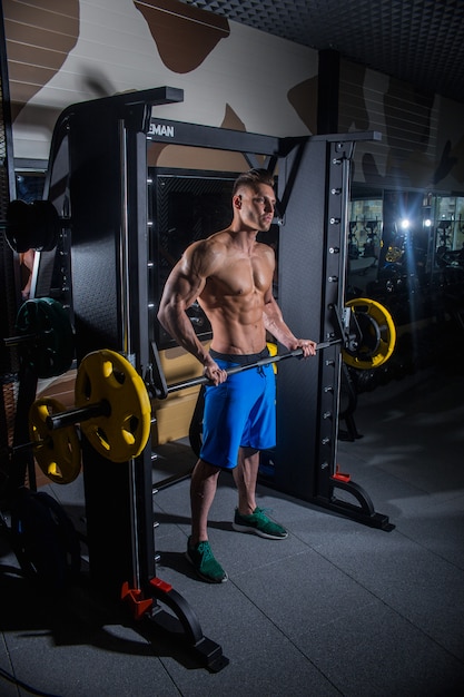 Sportowy mężczyzna z dużymi mięśniami i szerokimi plecami trenuje na siłowni