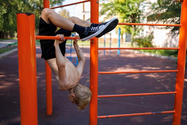 sportowy nastolatek zrobił backbend wiszący na poziomym pręcie Street workout na poziomym barze w parku szkolnym