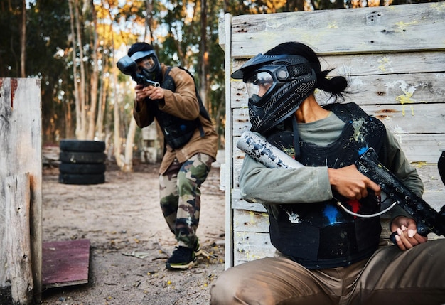 Sportowy paintball i kobieta z bronią do gry bitewnej lub zawodów na świeżym powietrzu na polu Walka wojenna armii wojskowej i żołnierza z bronią na strzelnicy, ukrywając się przed graczem do ćwiczeń