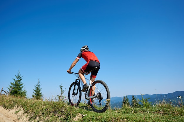 sportowy rowerzysta turystyczny w kasku i pełne wyposażenie rowerowe na trawiastym wzgórzu