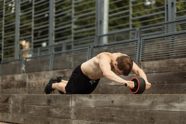 Sportowy sportowy kaukaski bez koszuli mężczyzna robi ćwiczenia z kołem rolkowym abs