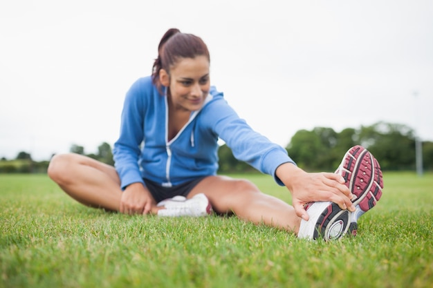 Sporty kobieta rozciąga jej nogę na trawie