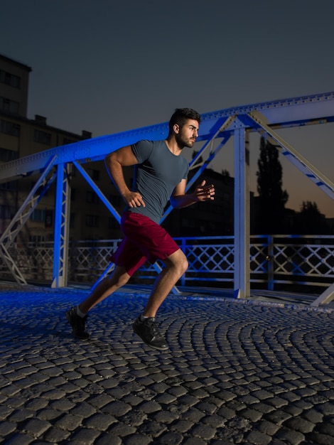 sporty miejskie, młody zdrowy mężczyzna biegający przez most w mieście wczesnym rankiem w nocy