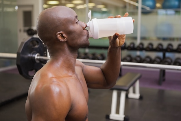 Sporty młody człowiek pije proteinę w gym