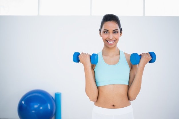Sporty uśmiechnięta kobieta podnosi błękitnych dumbbells