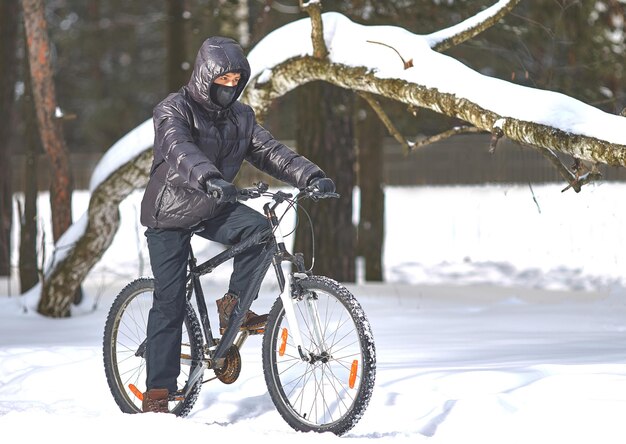 Sporty zimowe. Wycieczki rowerowe. Młody mężczyzna w czarnym ubraniu jeździ na rowerze