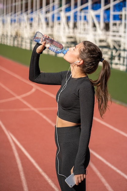 Spragniona, młoda, sprawna kobieta pije wodę z plastikowej butelki