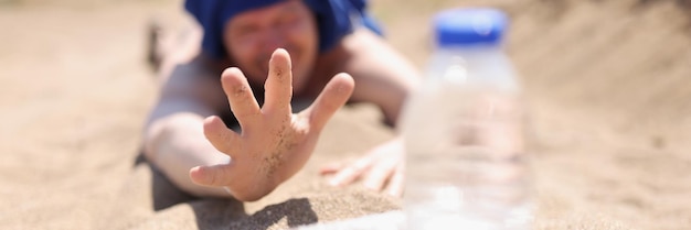 Spragniony mężczyzna leży na piasku sięgając po butelkę wody