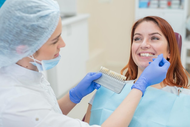 Sprawdź i wybierz kolor zębów w fotelu dentystycznym Dentysta wykonuje proces leczenia pięknej młodej rudowłosej dziewczyny Wybór implantu zęba