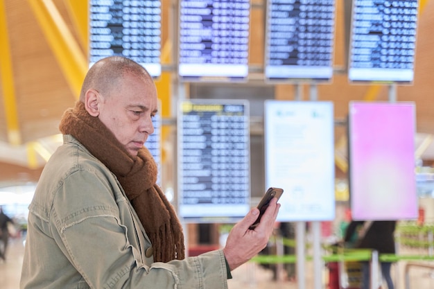 Sprawdzanie statusu lotu Mężczyzna spoglądający na telefon, a w tle wyświetlane są informacje o locie