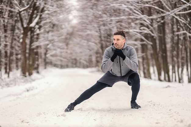 Sprawny sportowiec robi ćwiczenia rozgrzewające w śnieżny zimowy dzień w lesie.