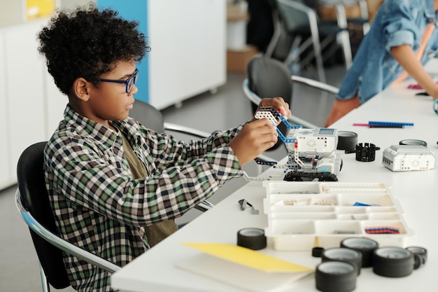 Sprytny afroamerykański uczeń konstruujący nowego robota przy biurku na lekcji