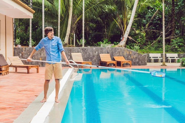 Sprzątacz basenu. Mężczyzna w niebieskiej koszuli ze sprzętem do czyszczenia basenów, słonecznie