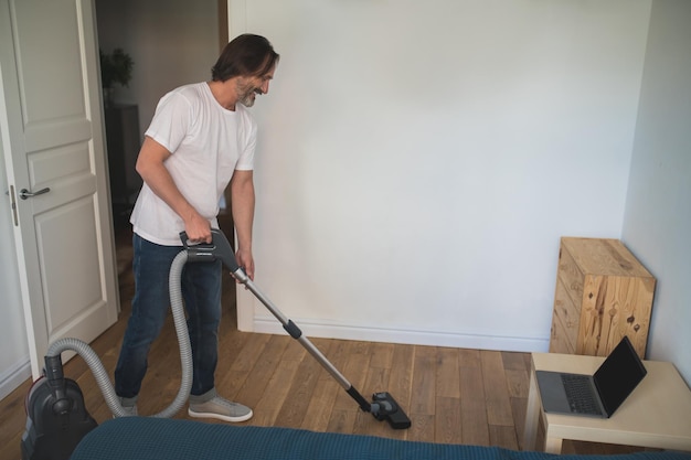 Zdjęcie sprzątanie domu. mężczyzna w białej koszulce robi odkurzanie i wygląda na zaangażowanego