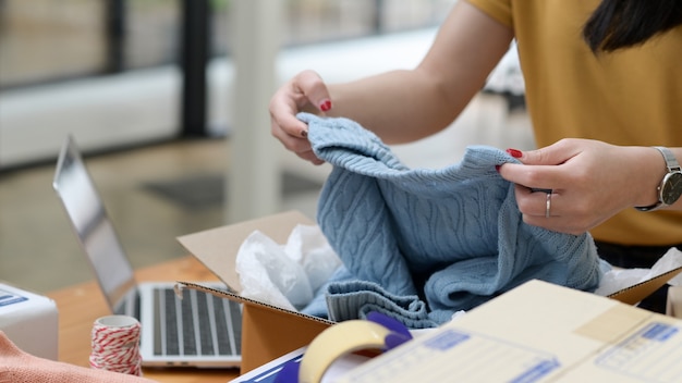 Sprzedająca online kobieta pakująca swetry w pudełka z dostawą do klientów, sprzedaż online, dostawa paczek.