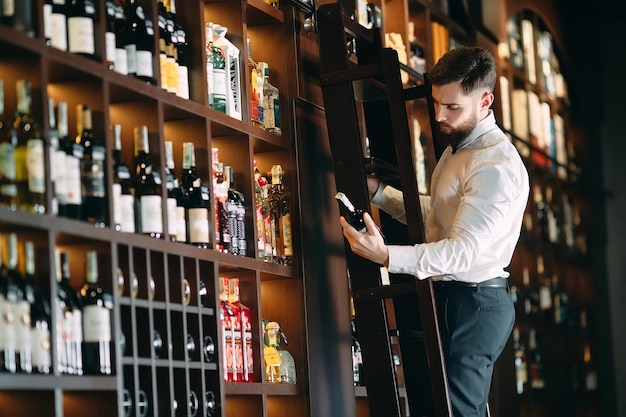 Zdjęcie sprzedawca napojów alkoholowych sortuje butelki stojące na drabinie.