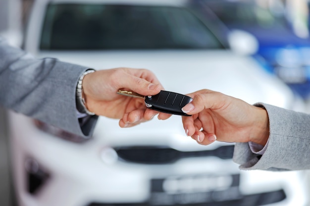Zdjęcie sprzedawca samochodów wręczający kluczyki do samochodu klientowi stojąc w salonie samochodowym.