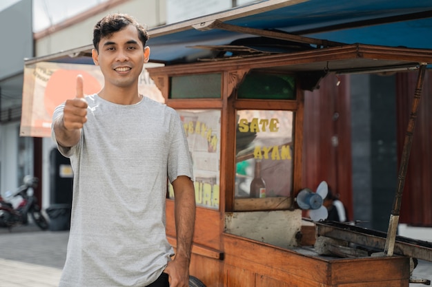 Sprzedawca ulicznego jedzenia z straganem z indonezyjskim kurczakiem satay gotującym na gorącym grillu na węgiel drzewny