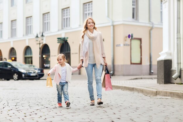 sprzedaż, konsumpcjonizm i koncepcja ludzi - szczęśliwa matka i dziecko z torbami na zakupy spacerującymi ulicą miasta