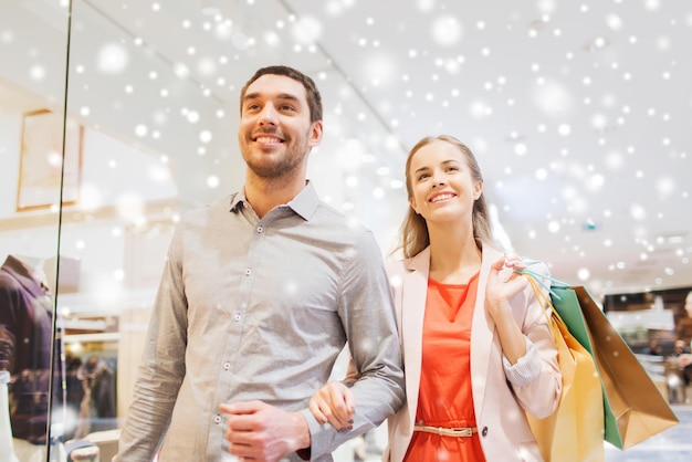 sprzedaż, konsumpcjonizm i koncepcja ludzi - szczęśliwa młoda para z torbami na zakupy spacerująca po centrum handlowym z efektem śniegu