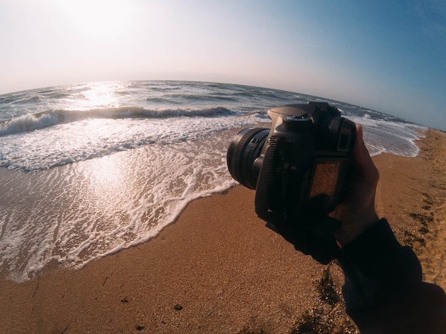 sprzęt do fotografii podróżniczej. styl życia artysty. letnia podróż. słoneczna plaża, piasek i morze. ręka trzyma aparat.