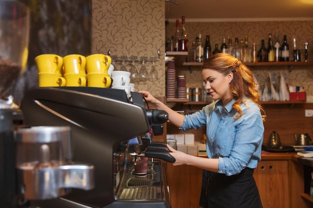 sprzęt, kawiarnia, koncepcja ludzi i technologii - kobieta barista robi kawę maszyną w kawiarni lub kuchni restauracji