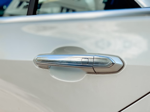 Srebrna klamka otwierająca drzwi pasażera auta w kolorze białym. Szczegóły samochodu z bliska.