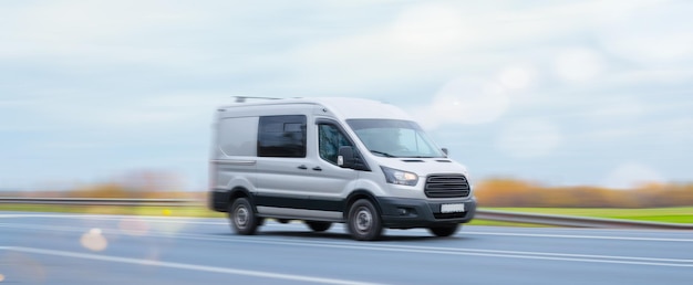 Zdjęcie srebrny minibus towarowy jadący autostradą poza krajobrazem miasta w połowie planu