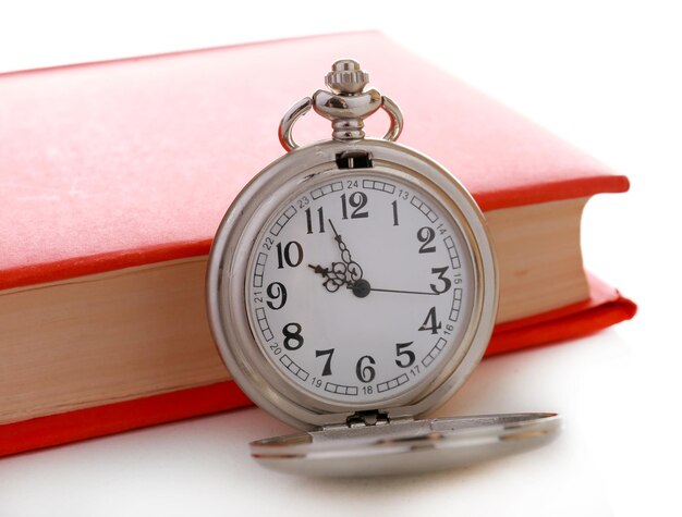 Srebrny zegar kieszonkowy i książka na białym stole
