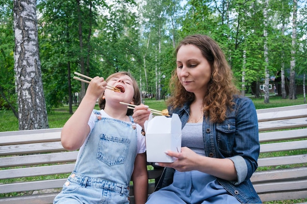 Średnio dorosła dojrzała kobieta i nastolatka na spacerze w letni dzień w parku je lunch z wokiem z makaronem