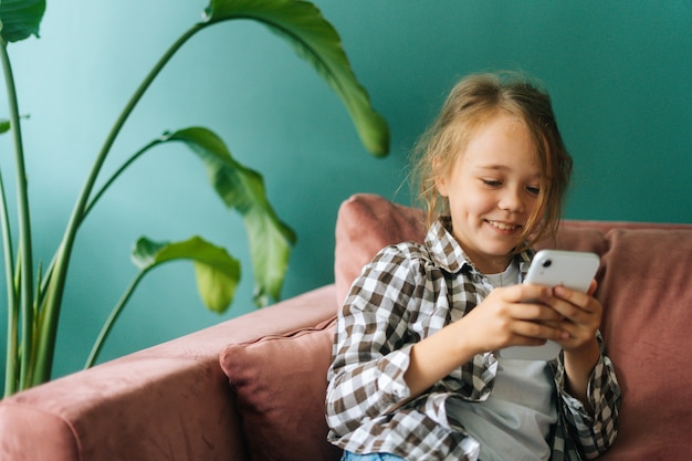 Średnio strzał portret wesołej ślicznej małej dziewczynki za pomocą smartfona, patrząc na oglądanie ekranu