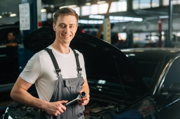 Średnio Ujęcie Portret Wesołego, Przystojnego, Młodego Mechanika, Mężczyzny W Mundurze, Trzymającego Specjalny Klucz...