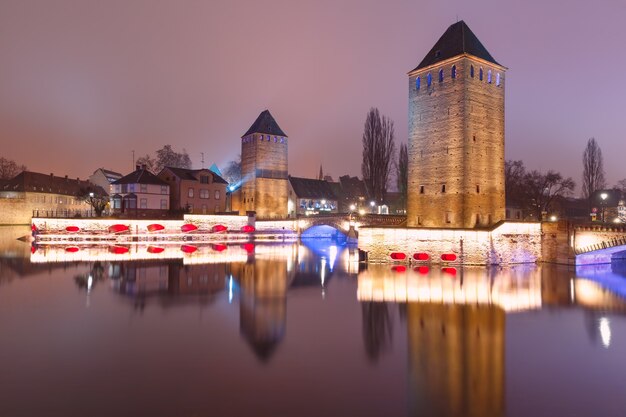 Średniowieczne wieże i mosty z lustrzanymi odbiciami w Petite France nocą, Strasburg, Alzacja, Francja