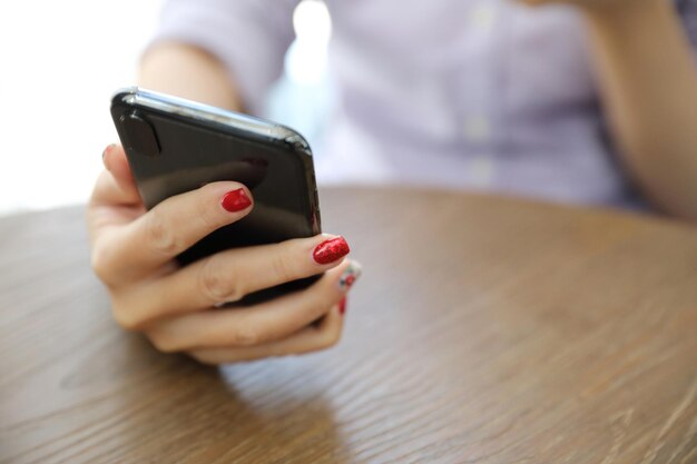Środkowa część kobiety używającej telefonu komórkowego przy stole