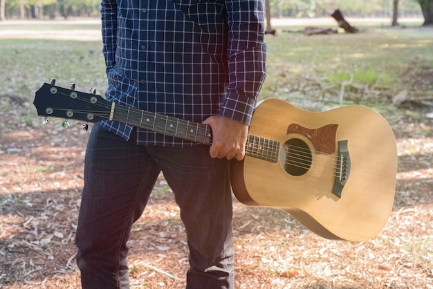 Środkowa część mężczyzny trzymającego gitarę stojącego w parku