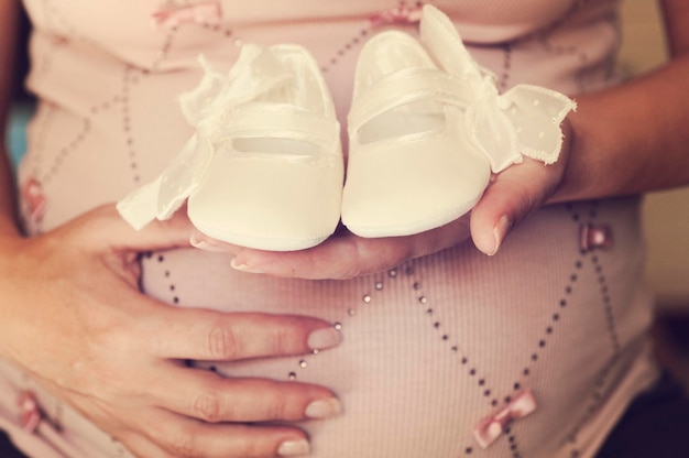 Środkowa sekcja ciężarnej kobiety trzymającej buty w domu