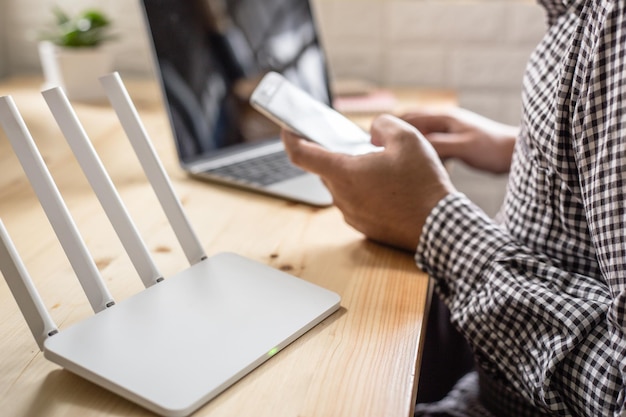 Zdjęcie Środkowa sekcja człowieka używającego laptopa i smartfona za pomocą routera na biurku w biurze